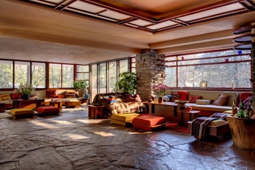 A cozy, modern living space with stone accents, large windows, and colorful seating arrangements surrounded by greenery.