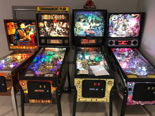 A row of colorful pinball machines featuring themes like Ghostbusters, Jurassic Park, and Bounty Hunter.