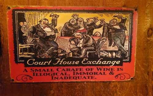 A vintage sign depicting a lively scene in a courtroom, with the text about wine being illogical, immoral, and inadequate.