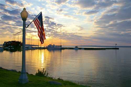 A serene sunset over a calm harbor, with an American flag and boats silhouetted against the colorful sky.