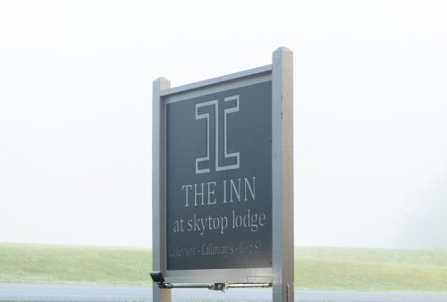 Sign for "The Inn at Skytop Lodge" partially obscured by fog, with green grass in the background.