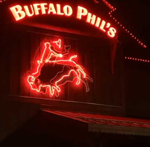 Neon sign of "Buffalo Phil's" featuring a cowboy and buffalo, illuminated at night.