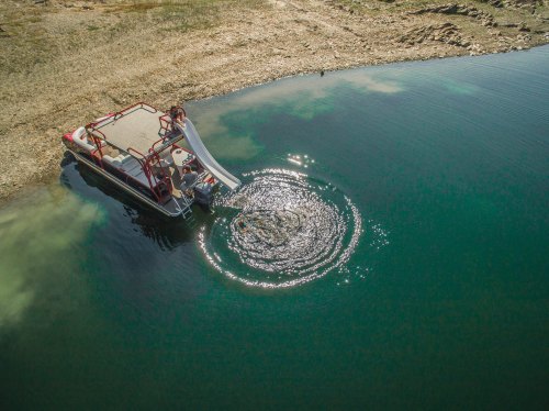 Aerial view of a boat on a calm lake, with a person sliding into the water, creating ripples.