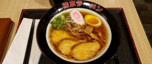 A bowl of ramen with sliced pork, a soft-boiled egg, green onions, and narutomaki, served on a black tray.
