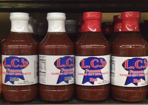 Four bottles of L.C.'s Famous Kansas City BBQ sauce, labeled Mild and Hot, displayed on a store shelf.