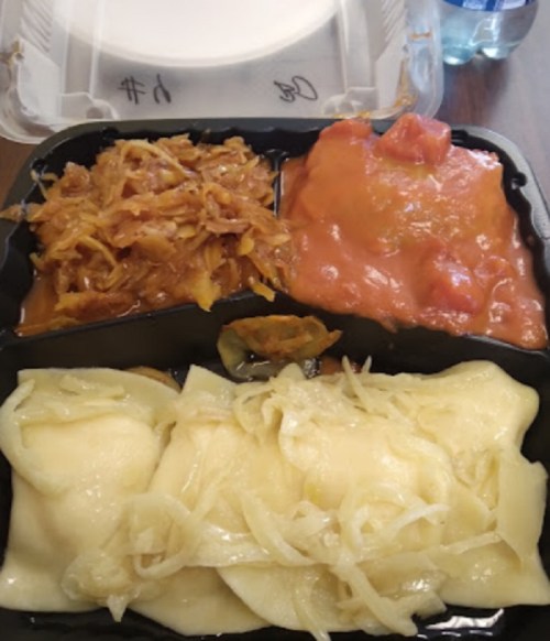 A takeout container with three compartments: dumplings with onions, sauerkraut, and a tomato-based dish.