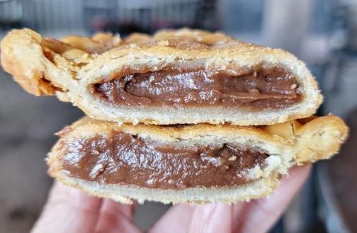 A hand holding two halves of a flaky pastry filled with rich chocolate cream.