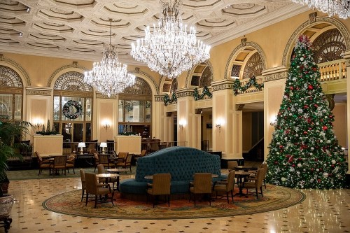 Elegant hotel lobby decorated for the holidays, featuring a large Christmas tree and chandeliers.