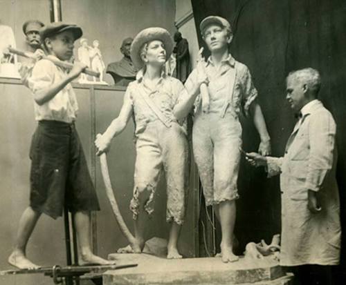 A historical black-and-white photo of boys posing with a sculptor and a clay statue in a studio setting.