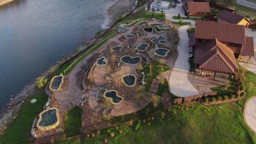 Aerial view of a landscaped area with multiple pools and a river, surrounded by greenery and buildings.