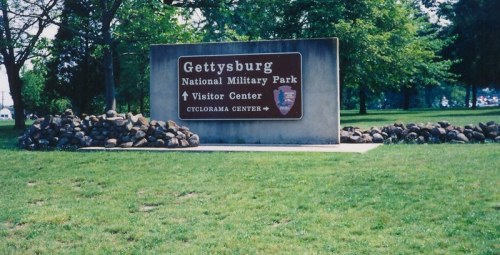 Sign for Gettysburg National Military Park, featuring directions to the Visitor Center and Cyclorama Center, surrounded by greenery.