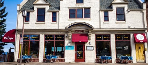 A charming restaurant exterior with red awnings, outdoor seating, and large windows showcasing the menu.
