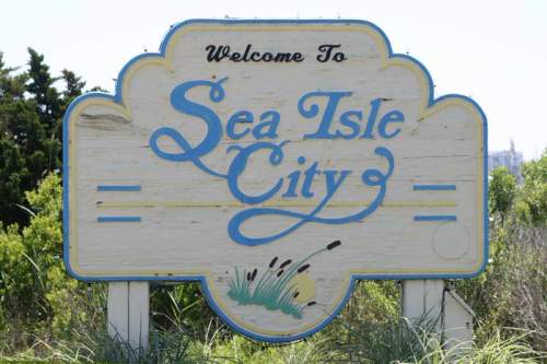 Welcome sign for Sea Isle City, featuring blue lettering and a decorative design against a natural backdrop.