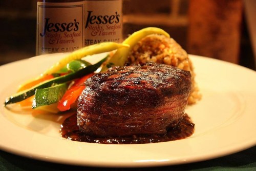 A perfectly cooked steak on a plate, accompanied by colorful vegetables and a side of rice, with a bottle of steak sauce.