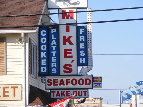 Sign for Mike's Seafood Takeout featuring "Cooked Platters" and "Fresh" in bold letters.