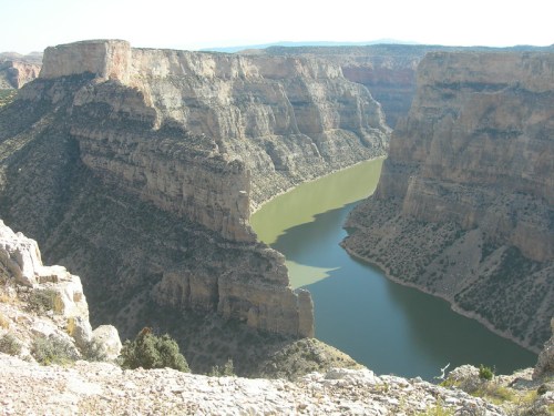 A winding river flows through steep, rocky cliffs in a vast canyon landscape under a clear sky.