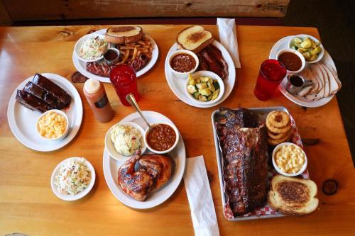 A spread of barbecue dishes including ribs, chicken, sides, and drinks on a wooden table.