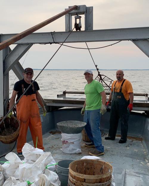 Three fishermen on a boat, preparing equipment and baskets for fishing, with water in the background.