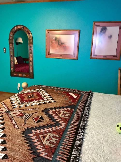 A vibrant turquoise wall with framed art, a mirror, and a patterned blanket on a bed.