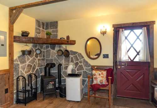 Cozy interior with a stone wall, wooden accents, a small stove, and a red door, creating a warm, inviting atmosphere.