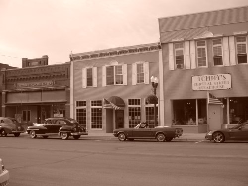 Historic downtown scene featuring vintage cars parked in front of charming storefronts, including a steakhouse.