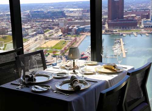 Elegant dining table set with fine china and glassware, overlooking a scenic city and waterfront view.