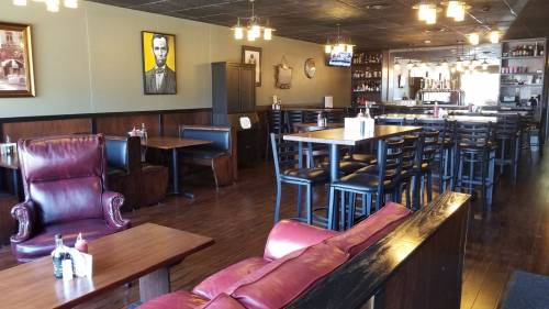 A cozy restaurant interior featuring wooden tables, leather chairs, and a portrait of Abraham Lincoln on the wall.