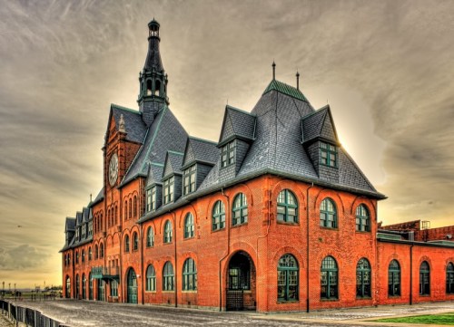 Historic red brick building with a clock tower, featuring intricate architectural details against a cloudy sky.