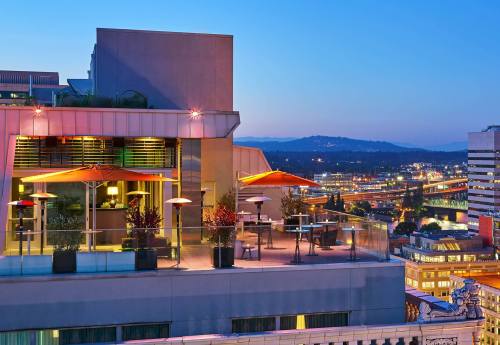 Rooftop terrace with orange umbrellas, overlooking a city skyline at dusk, with lights twinkling in the background.