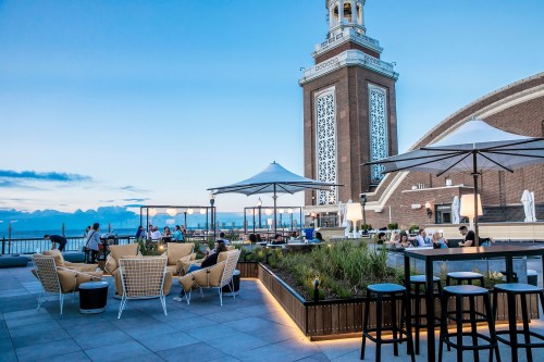 Rooftop lounge with modern seating, umbrellas, and a view of a tower at dusk, creating a relaxed atmosphere.