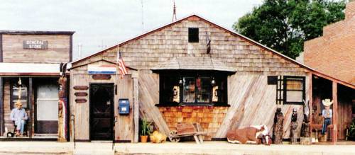 A rustic wooden building with a porch, featuring cowboy decor and an American flag, set in a small town.