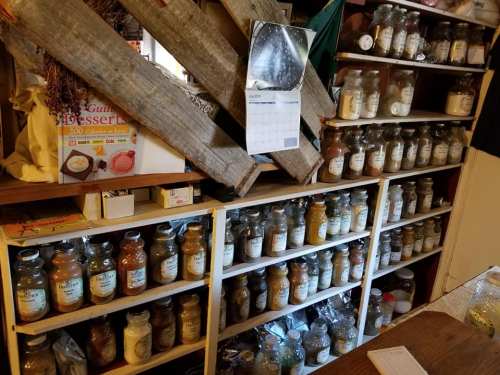 A wooden shelf filled with jars of various spices and ingredients, with a calendar hanging above.
