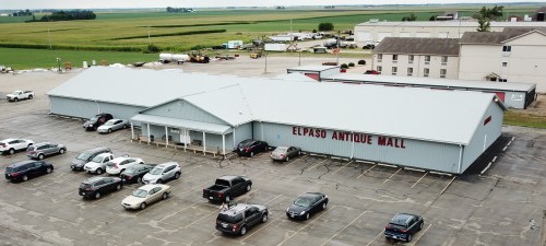 Aerial view of El Paso Antique Mall with parked cars and green fields in the background.