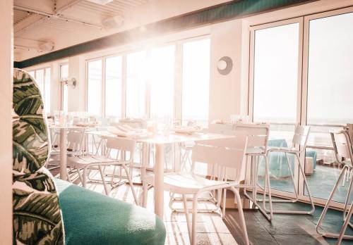 Bright, airy restaurant interior with white tables and chairs, large windows, and sunlight streaming in.