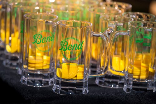 Clear mugs with green "Bend" logo and yellow tokens inside, arranged on a table.