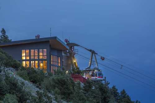 A mountain cable car station at dusk, with a gondola approaching and trees surrounding the building.
