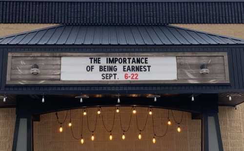 Sign announcing "The Importance of Being Earnest" performance dates: September 6-22, with decorative lights below.