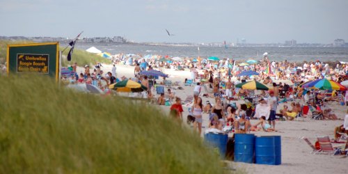 Crowded beach scene with umbrellas, boogie boards, and people enjoying the sun and water.