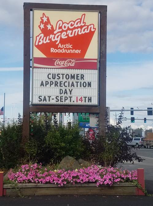 Sign for Local Burgerman advertising Customer Appreciation Day on September 14th, surrounded by flowers.