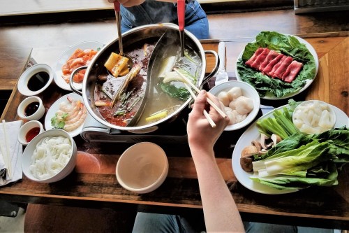 A table set for hot pot with various ingredients, including meats, vegetables, and dipping sauces, ready to be cooked.
