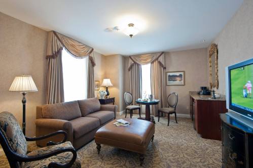 A cozy hotel room featuring a sofa, coffee table, TV, and elegant decor with soft lighting and curtains.