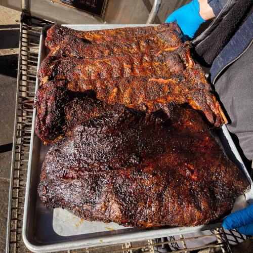 A tray of smoked meats, including ribs and a large brisket, with a charred, flavorful crust.