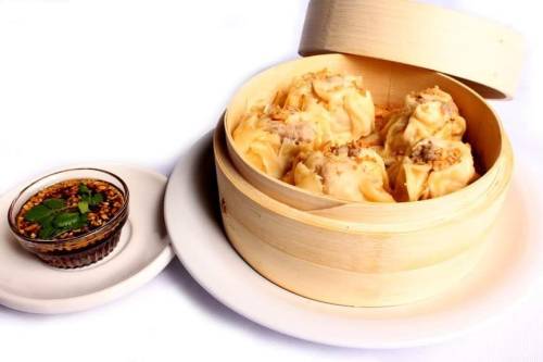A bamboo steamer filled with dumplings, accompanied by a small bowl of dipping sauce and garnished with herbs.