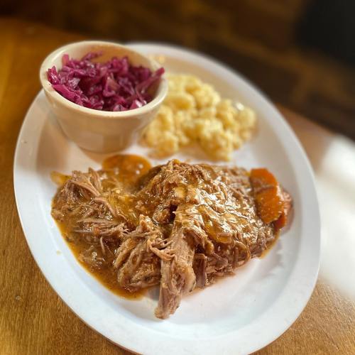 A plate with pulled pork in gravy, served with macaroni and cheese and a side of purple coleslaw.