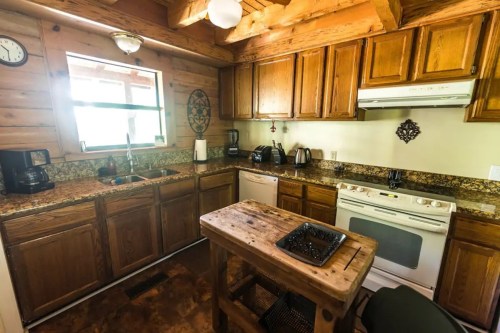 Cozy kitchen with wooden cabinets, granite countertops, and a rustic table, featuring appliances and a window for natural light.