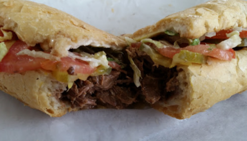 A close-up of a sandwich filled with shredded beef, lettuce, tomatoes, and pickles, cut in half.
