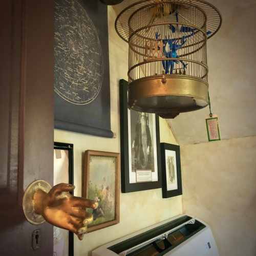 A hand-shaped door handle leads to a room with a hanging light fixture and various framed artworks on the walls.