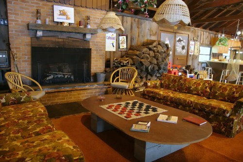 Cozy rustic living room with a fireplace, floral sofas, a checkers table, and wooden decor.