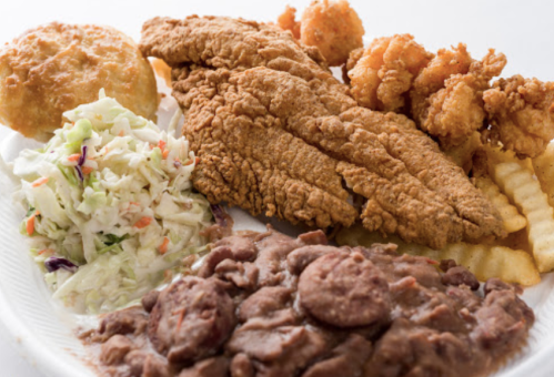 A plate of fried fish, shrimp, coleslaw, French fries, and a biscuit, served with a side of refried beans.