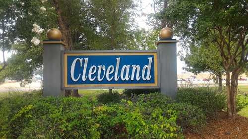 Sign for Cleveland, featuring blue background with gold lettering, surrounded by greenery and trees.